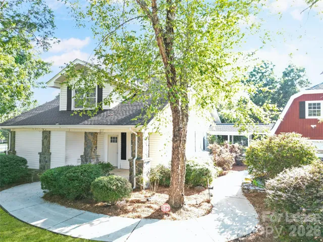 Welcoming front entry with timeless stone accents, mature shade trees, and a covered walkway leading to the home's private courtyard and detached garage.