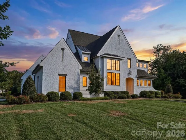 Impressive exterior showcases timeless white-brick architecture, manicured landscaping, and a spacious two-car garage with a broad driveway for convenient parking and access.