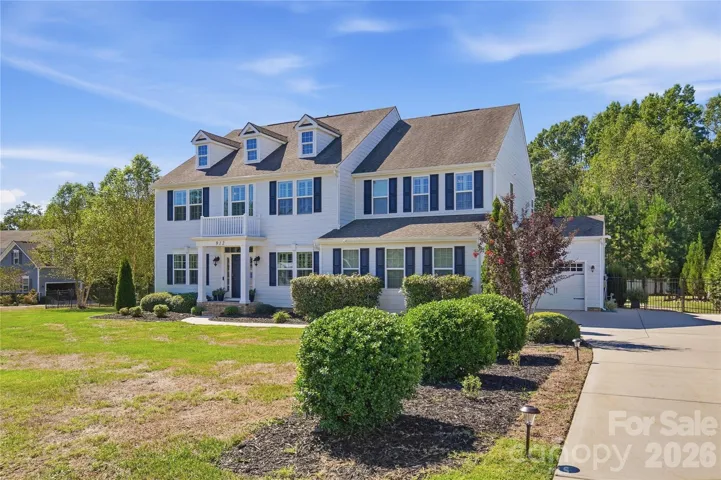 Georgian Colonial with a columned front portico, mature landscaping, and an expanded driveway leading to the split three-car garage.