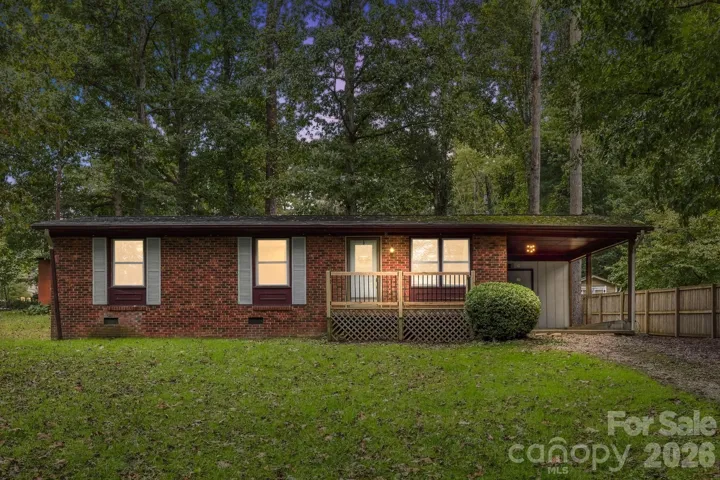 Twilight exterior view of this classic brick home, surrounded by mature trees with a covered carport and welcoming front entry.