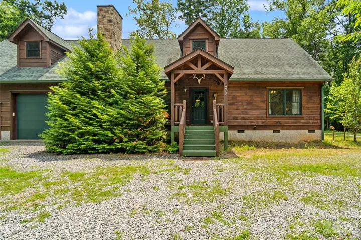 Classic Pisgah Forest cabin living. The inviting  exterior showcases rustic wood siding, a green shingled roof with dormer accents, and a covered entryway complete with custom timber detailing.