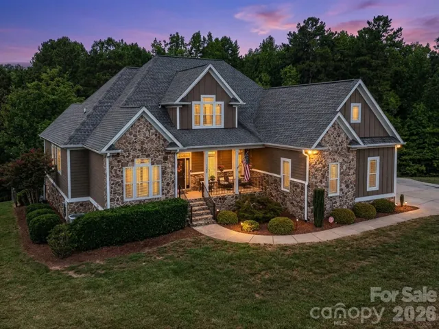 A striking stone-and-siding exterior showcases timeless architecture, a welcoming covered front porch, beautifully maintained landscaping, and impressive curb appeal.