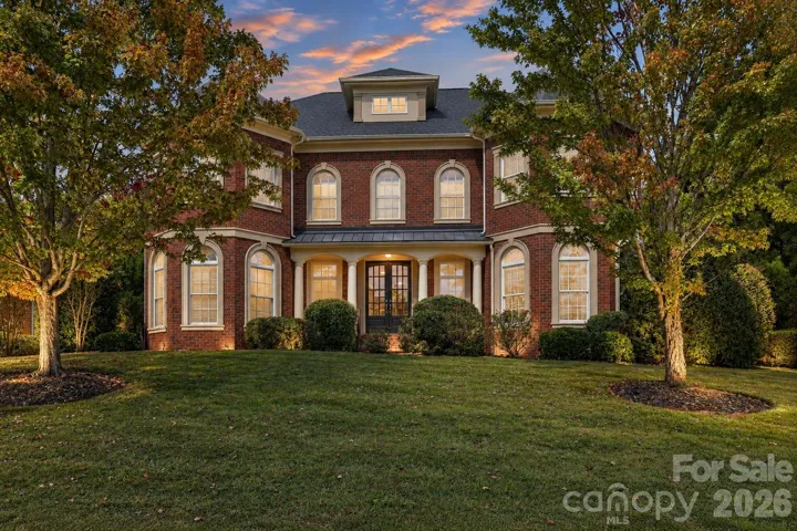 A striking evening view highlights this full-brick Weddington Chase home framed by mature trees and  established landscaping.