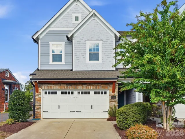 Front exterior of 337 Belton St, a 2019 end-unit townhome in Charlotte, NC 28209 near South End. Craftsman-inspired facade with shake siding, stacked stone accents, carriage-style two-car garage door, and mature landscaping.