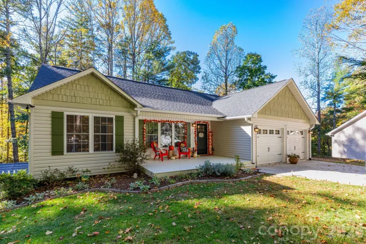 Inviting exterior featuring a covered front porch, attached two-car garage, landscaped planting beds, and a wooded backdrop.
