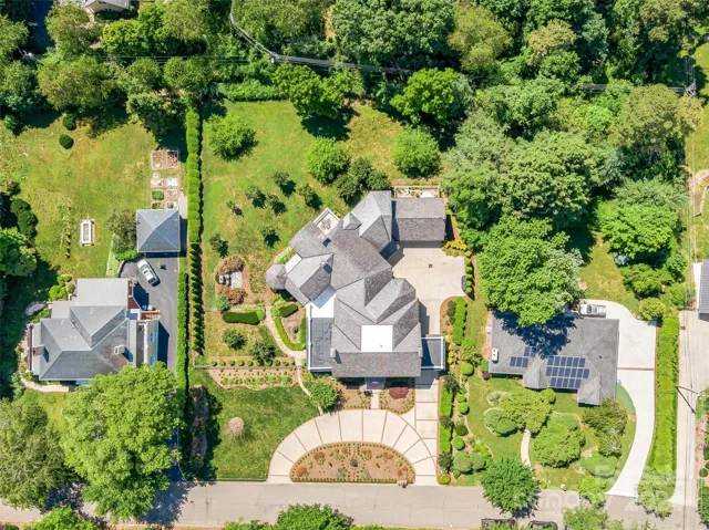 A bird's eye perspective of: the professional landscaping (with auto irrigation) that encompasses this residence, the artistic front curb appeal thanks to the elaborate hardscaping, the historic porte cochere on the right side of the home, the built-in brick outdoor fireplace on the left side of the home, and - of course - a view of the fenced backside yard.