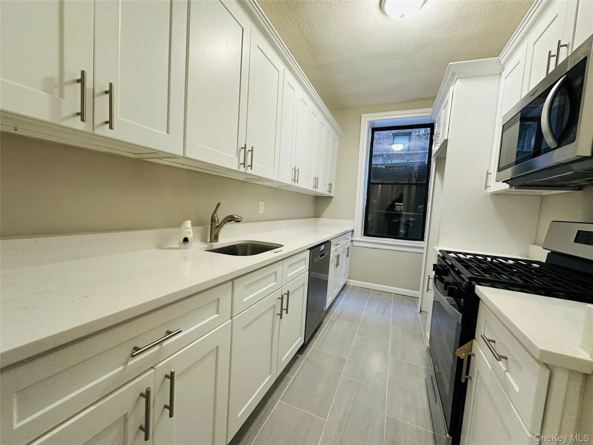 Kitchen with white cabinetry, sink, stainless steel appliances, and a textured ceiling Kitchen with white cabinetry, sink, stainless steel appliances, and a textured ceiling