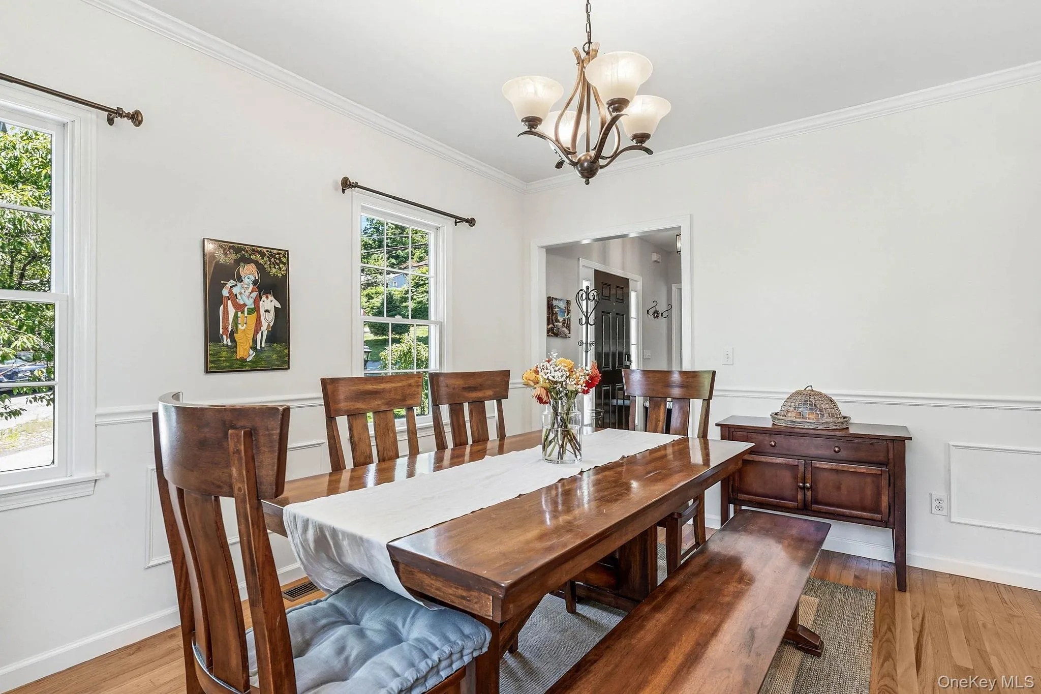 Dining area featuring wood-finish flooring, white paneled wainscoting, crown molding, and a bronze chandelier Dining area featuring wood-finish flooring, white paneled wainscoting, crown molding, and a bronze chandelier