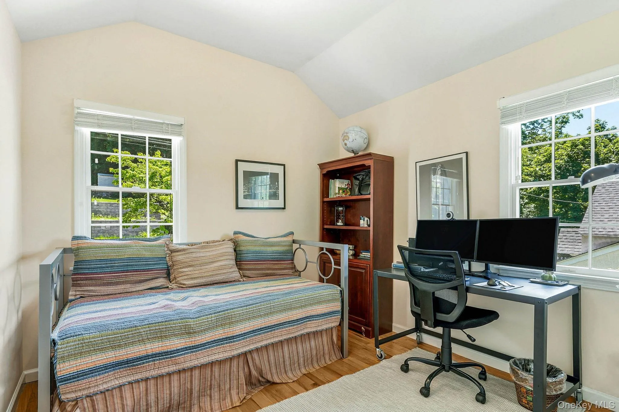 Room featuring vaulted ceilings, two windows with gridded panes, light-toned wall paint, and wood-finish flooring Room featuring vaulted ceilings, two windows with gridded panes, light-toned wall paint, and wood-finish flooring