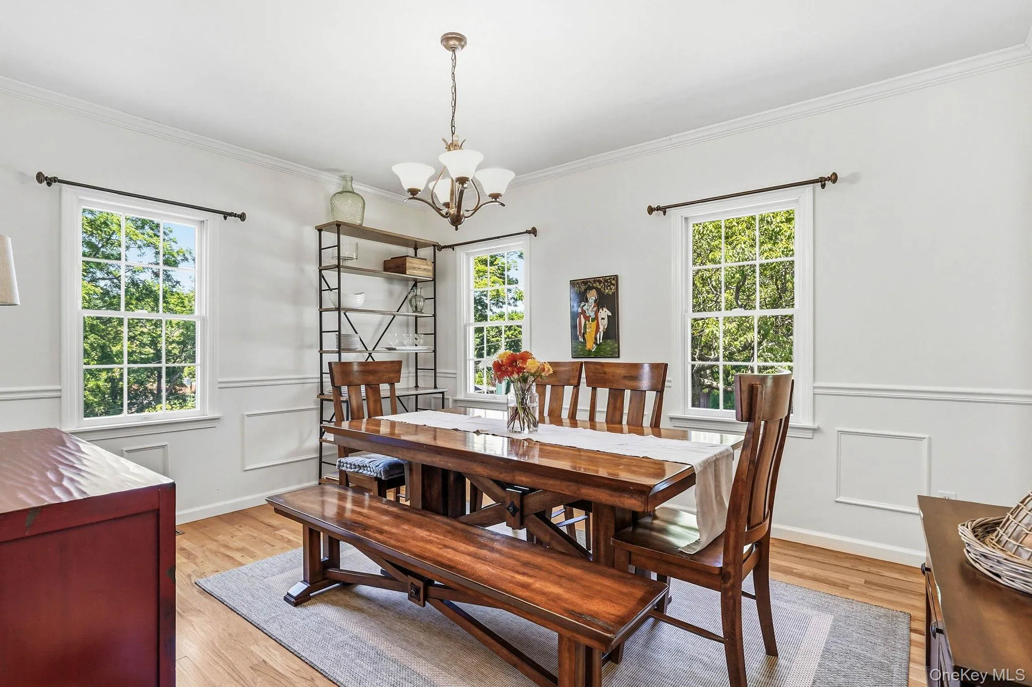 Dining space featuring light wood-finish flooring, white paneled walls, and multiple double-hung windows Dining space featuring light wood-finish flooring, white paneled walls, and multiple double-hung windows