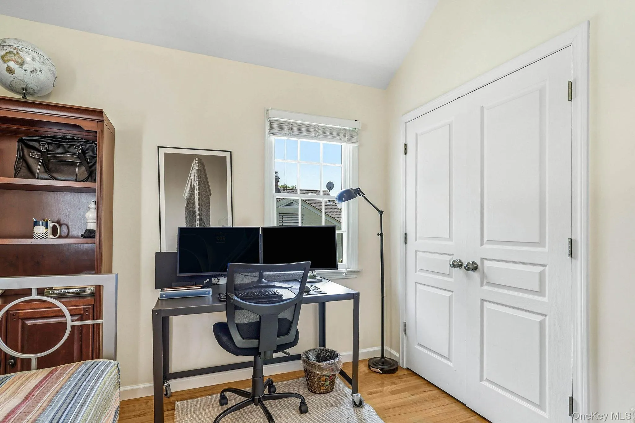Light-toned walls with a vaulted ceiling, wood-finish flooring, a double-panel door, and a built-in wooden shelving unit Light-toned walls with a vaulted ceiling, wood-finish flooring, a double-panel door, and a built-in wooden shelving unit