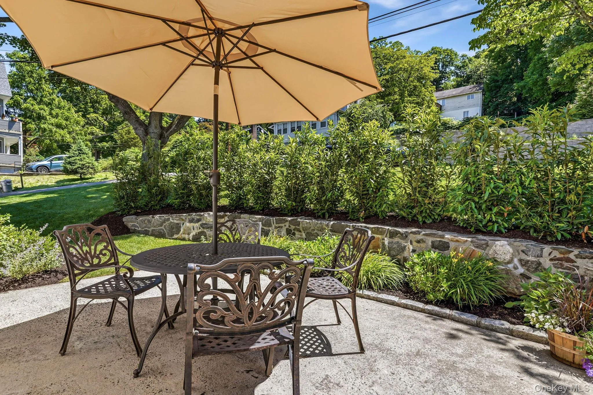 Paved patio space featuring a natural stone retaining wall, bordering lush landscaping and mature trees Paved patio space featuring a natural stone retaining wall, bordering lush landscaping and mature trees