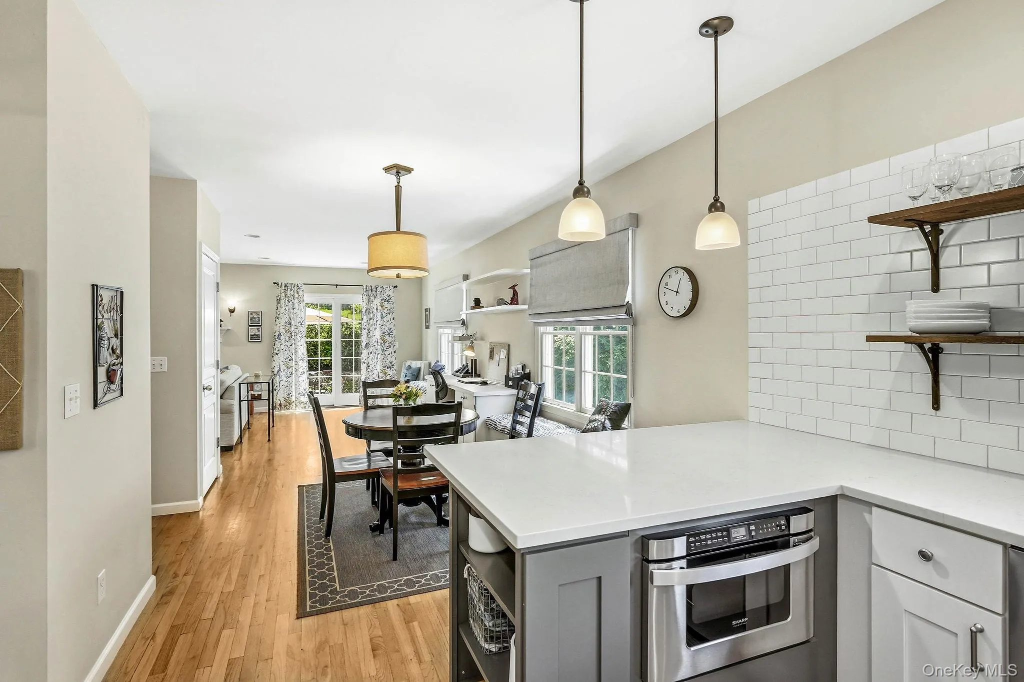 Open-concept kitchen featuring a peninsula with light-toned countertops, white subway tile backsplash, and two pendant lights Open-concept kitchen featuring a peninsula with light-toned countertops, white subway tile backsplash, and two pendant lights