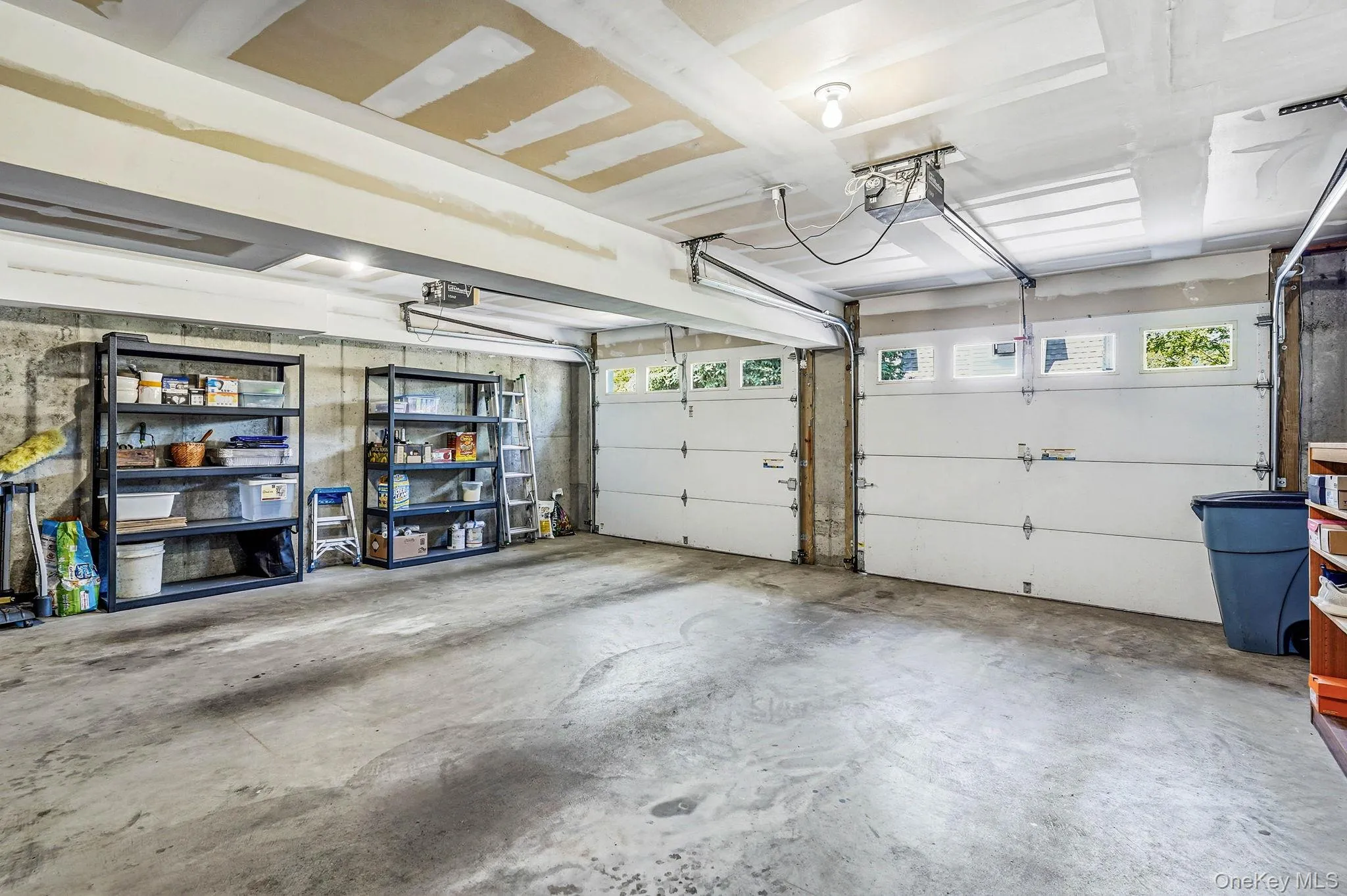 Two-car garage featuring concrete flooring, exposed concrete foundation walls, and two white garage doors with upper window panels Two-car garage featuring concrete flooring, exposed concrete foundation walls, and two white garage doors with upper window panels