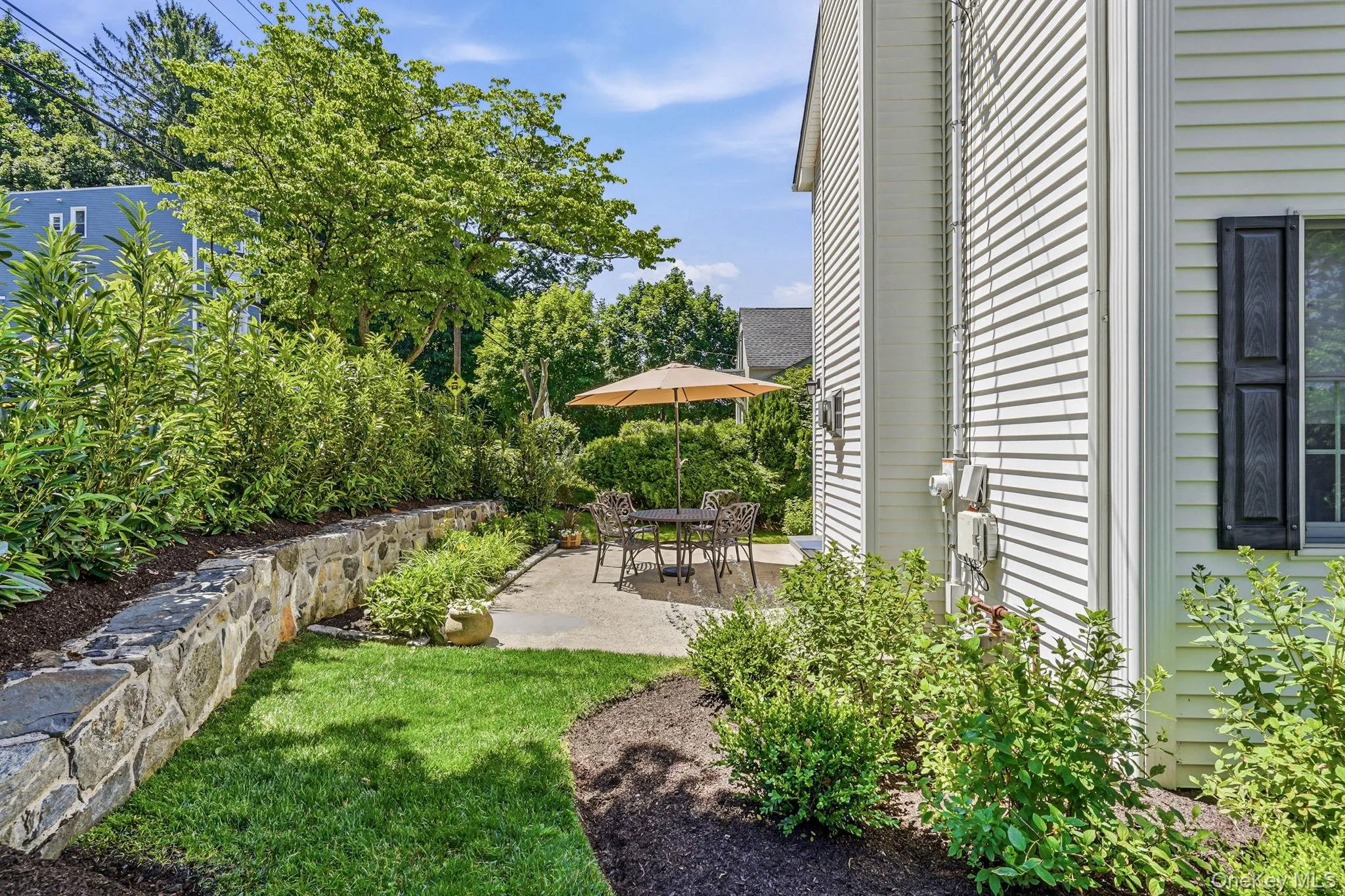 Private side patio featuring a stone retaining wall and lush landscaping Private side patio featuring a stone retaining wall and lush landscaping