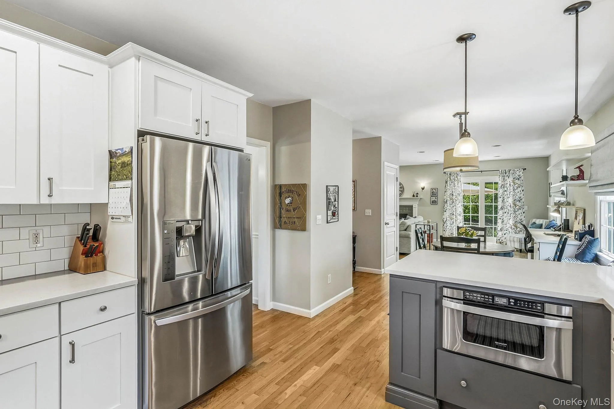 Kitchen featuring wood-finish flooring, white shaker cabinetry, an undermount sink, a white subway tile backsplash, and an island with pendant lighting and an integrated microwave Kitchen featuring wood-finish flooring, white shaker cabinetry, an undermount sink, a white subway tile backsplash, and an island with pendant lighting and an integrated microwave