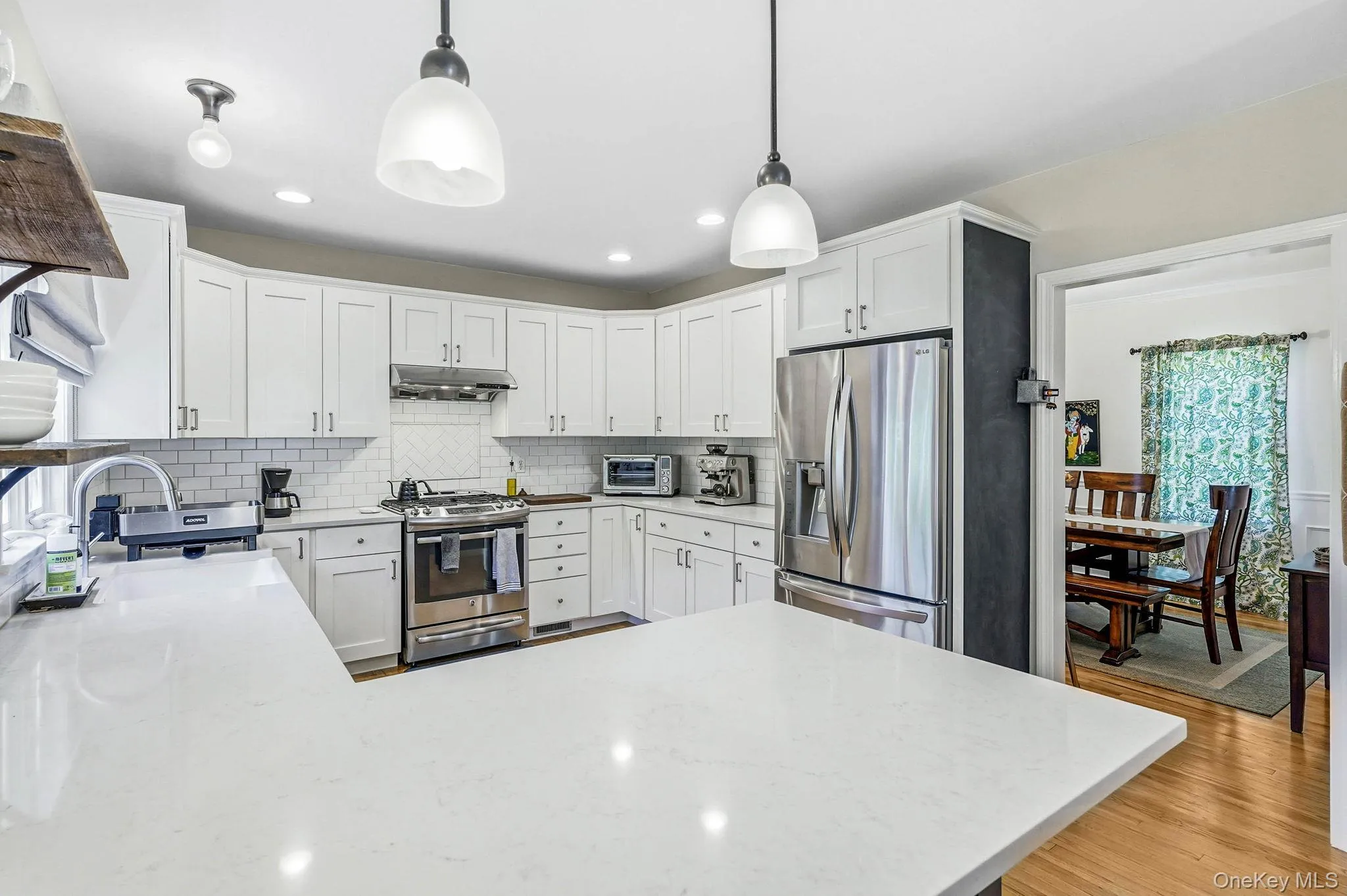 Kitchen featuring white shaker cabinetry, stainless steel appliances, a subway tile backsplash, light-toned countertops, and hardwood flooring Kitchen featuring white shaker cabinetry, stainless steel appliances, a subway tile backsplash, light-toned countertops, and hardwood flooring