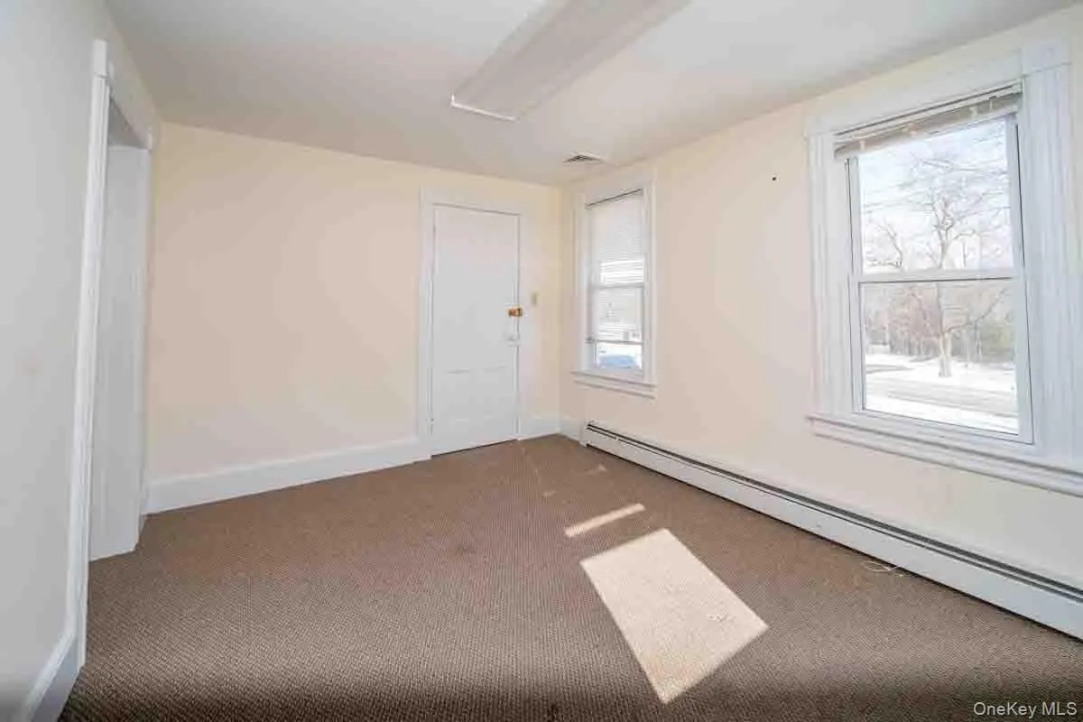 Carpeted empty room with plenty of natural light, baseboards, and a baseboard heating unit Carpeted empty room with plenty of natural light, baseboards, and a baseboard heating unit