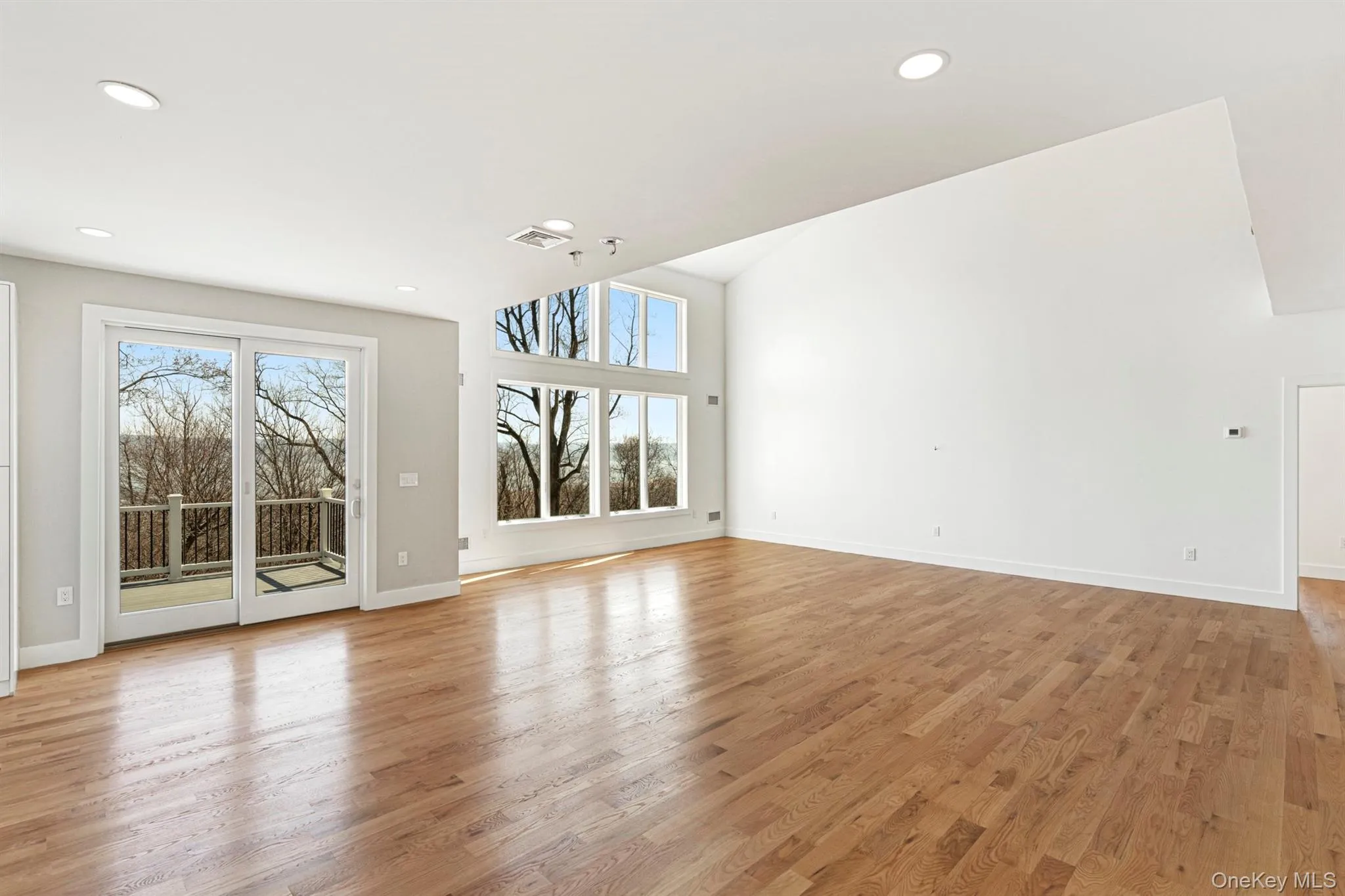 Unfurnished living room with wood finished floors, lofted ceiling, and recessed lighting Unfurnished living room with wood finished floors, lofted ceiling, and recessed lighting