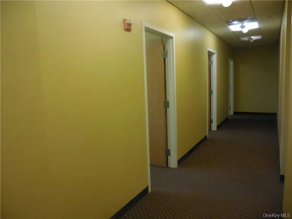 Hallway with a paneled ceiling and dark carpet Hallway with a paneled ceiling and dark carpet