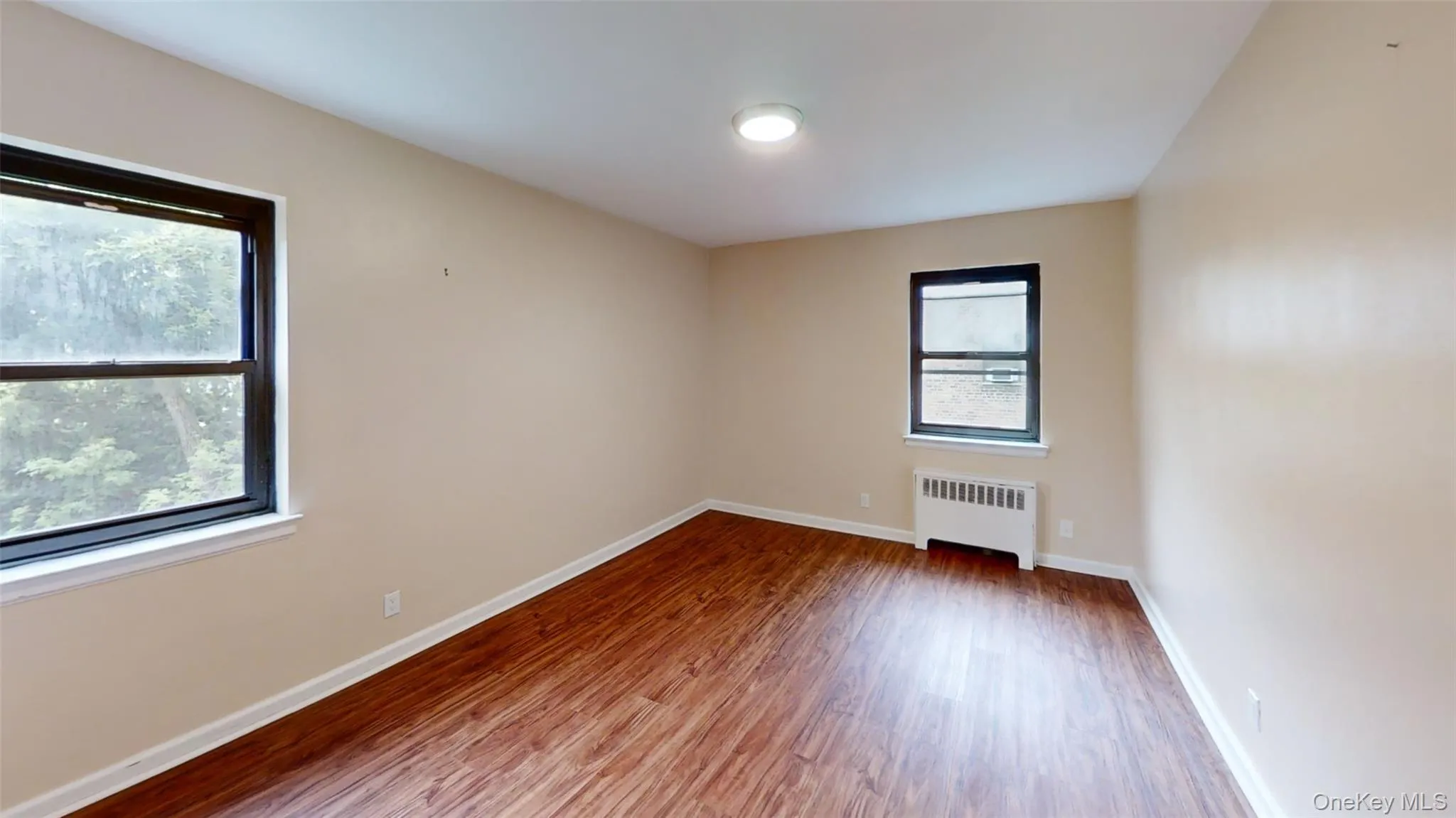 Empty room with radiator heating unit, wood finished floors, and baseboards Empty room with radiator heating unit, wood finished floors, and baseboards