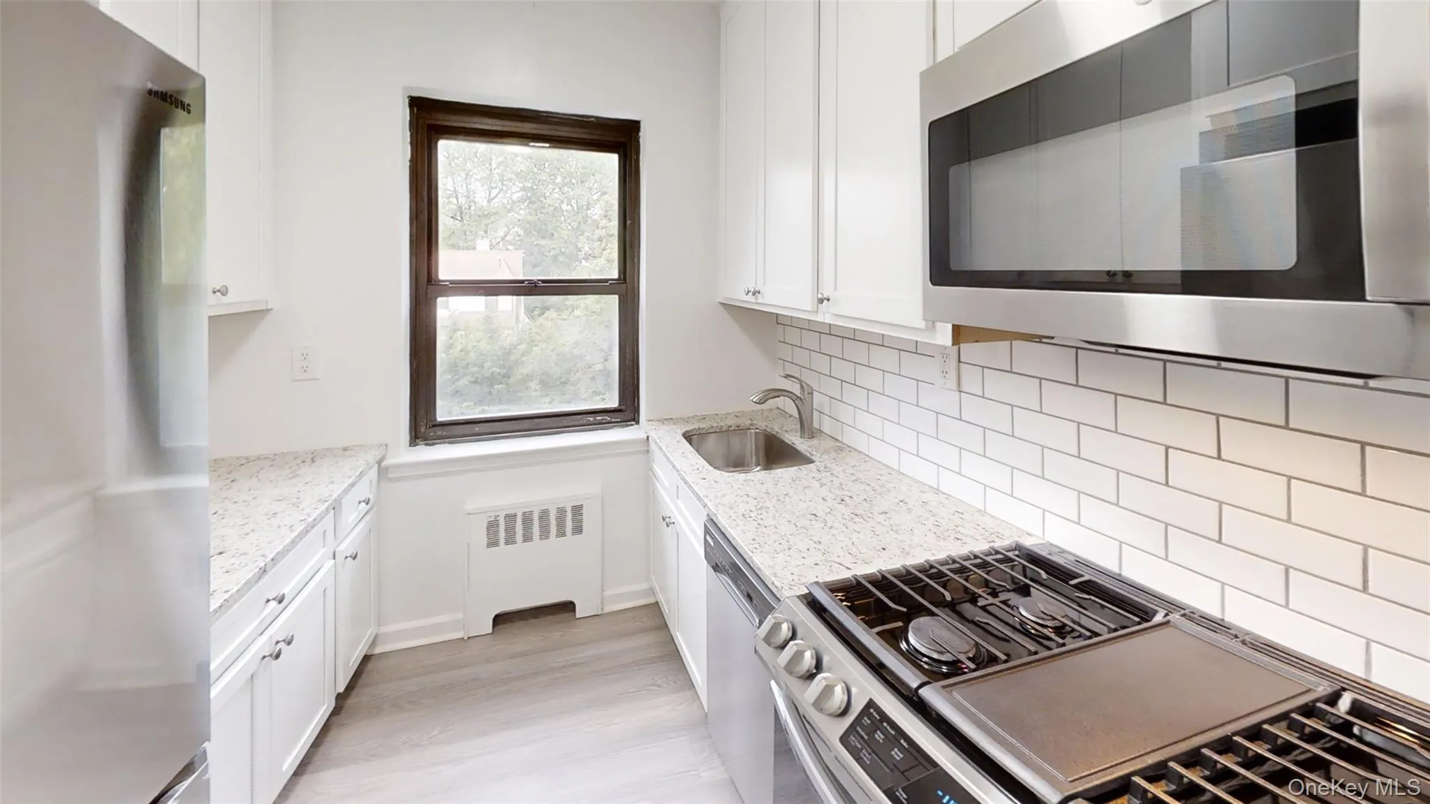 Kitchen with appliances with stainless steel finishes, radiator heating unit, white cabinetry, light stone countertops, and light wood-type flooring Kitchen with appliances with stainless steel finishes, radiator heating unit, white cabinetry, light stone countertops, and light wood-type flooring