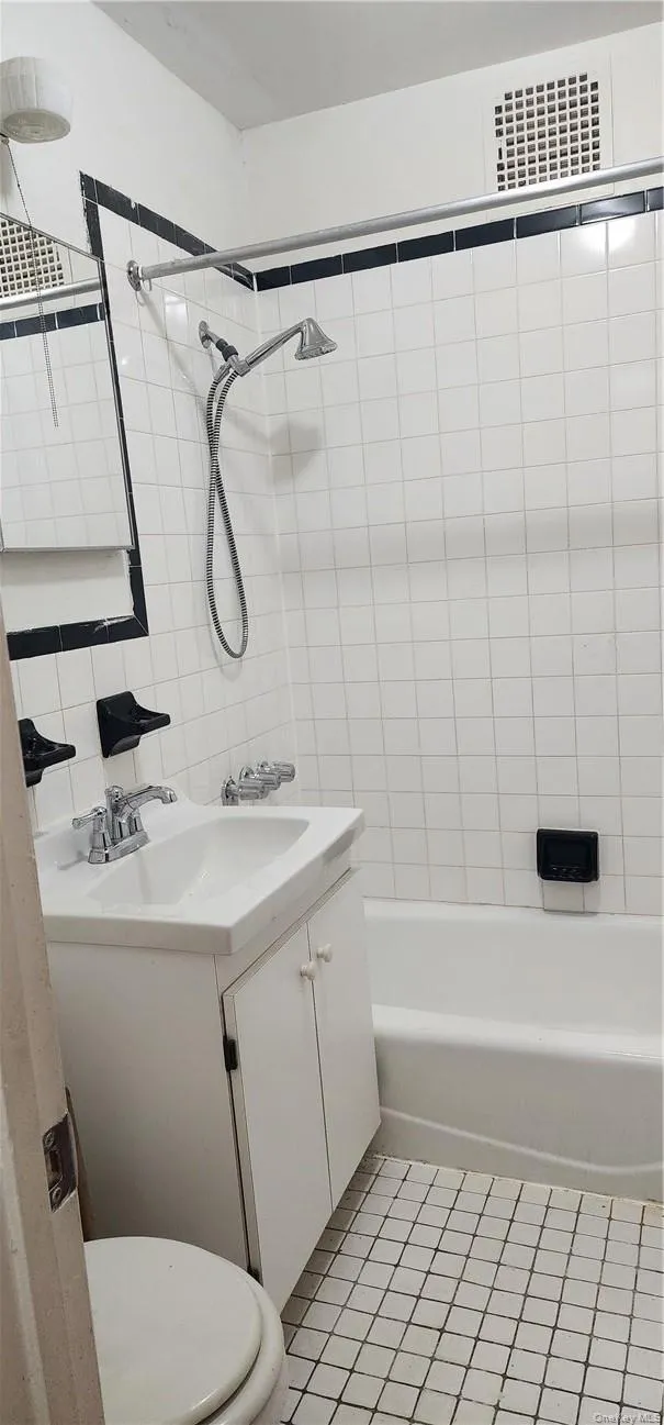 Full bathroom featuring tile walls, tiled shower / bath, tile floors, toilet, and vanity Full bathroom featuring tile walls, tiled shower / bath, tile floors, toilet, and vanity