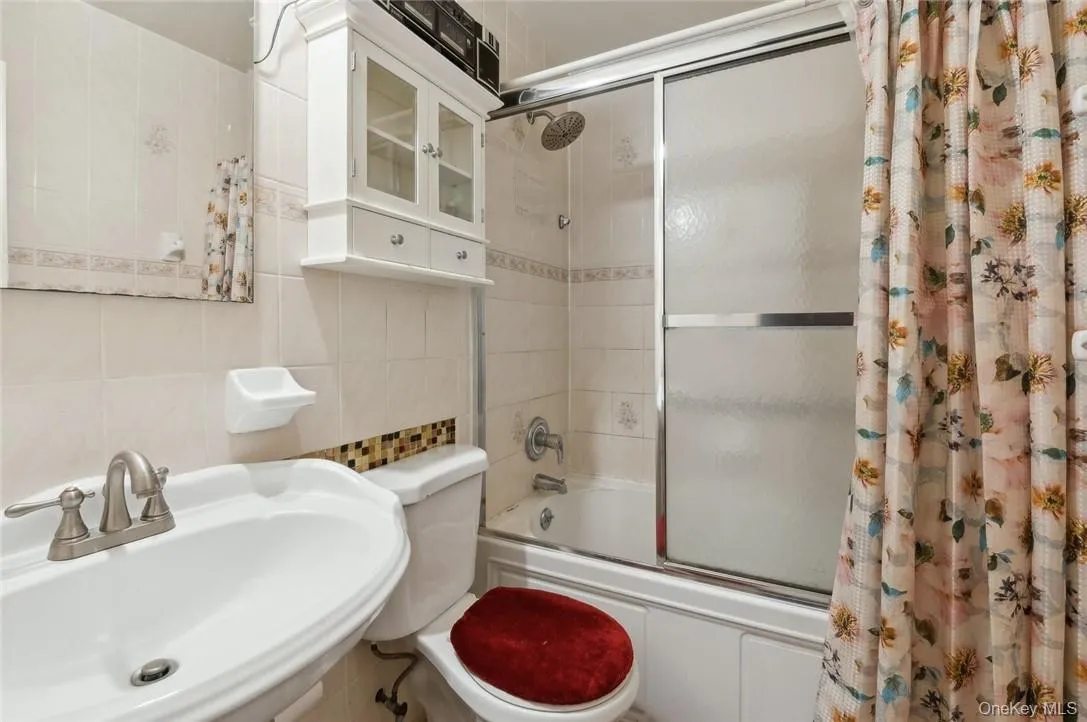 Full bathroom featuring shower / bathtub combination with curtain, sink, tile walls, and toilet Full bathroom featuring shower / bathtub combination with curtain, sink, tile walls, and toilet