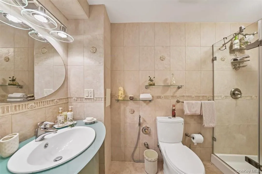 Bathroom featuring sink, an enclosed shower, tile walls, and toilet Bathroom featuring sink, an enclosed shower, tile walls, and toilet
