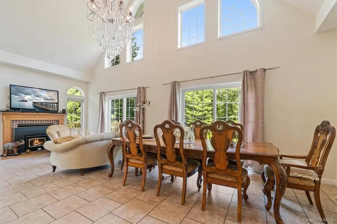 Tiled dining room with an inviting chandelier, a brick fireplace, a healthy amount of sunlight, and a towering ceiling Tiled dining room with an inviting chandelier, a brick fireplace, a healthy amount of sunlight, and a towering ceiling