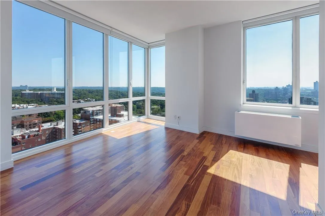 Empty room with plenty of natural light, a wall of windows, dark hardwood / wood-style flooring, and radiator heating unit Empty room with plenty of natural light, a wall of windows, dark hardwood / wood-style flooring, and radiator heating unit