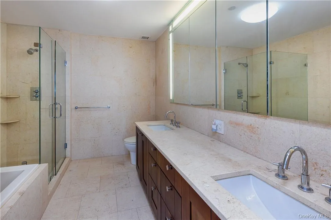Full bathroom with shower with separate bathtub, tile patterned floors, double sink vanity, tile walls, and toilet Full bathroom with shower with separate bathtub, tile patterned floors, double sink vanity, tile walls, and toilet