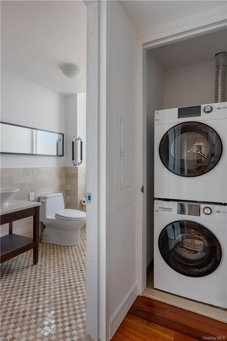 Laundry room featuring stacked washer and clothes dryer, electric panel, hardwood / wood-style floors, and tile walls Laundry room featuring stacked washer and clothes dryer, electric panel, hardwood / wood-style floors, and tile walls