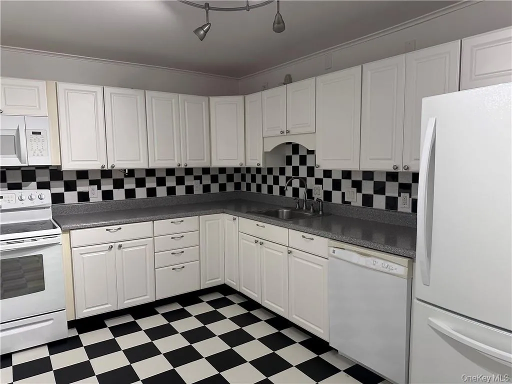 Kitchen with white appliances, rail lighting, white cabinets, backsplash, and sink Kitchen with white appliances, rail lighting, white cabinets, backsplash, and sink