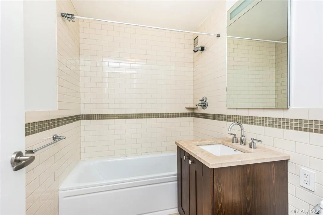 Bathroom featuring vanity, tile walls, tiled shower / bath, and backsplash Bathroom featuring vanity, tile walls, tiled shower / bath, and backsplash