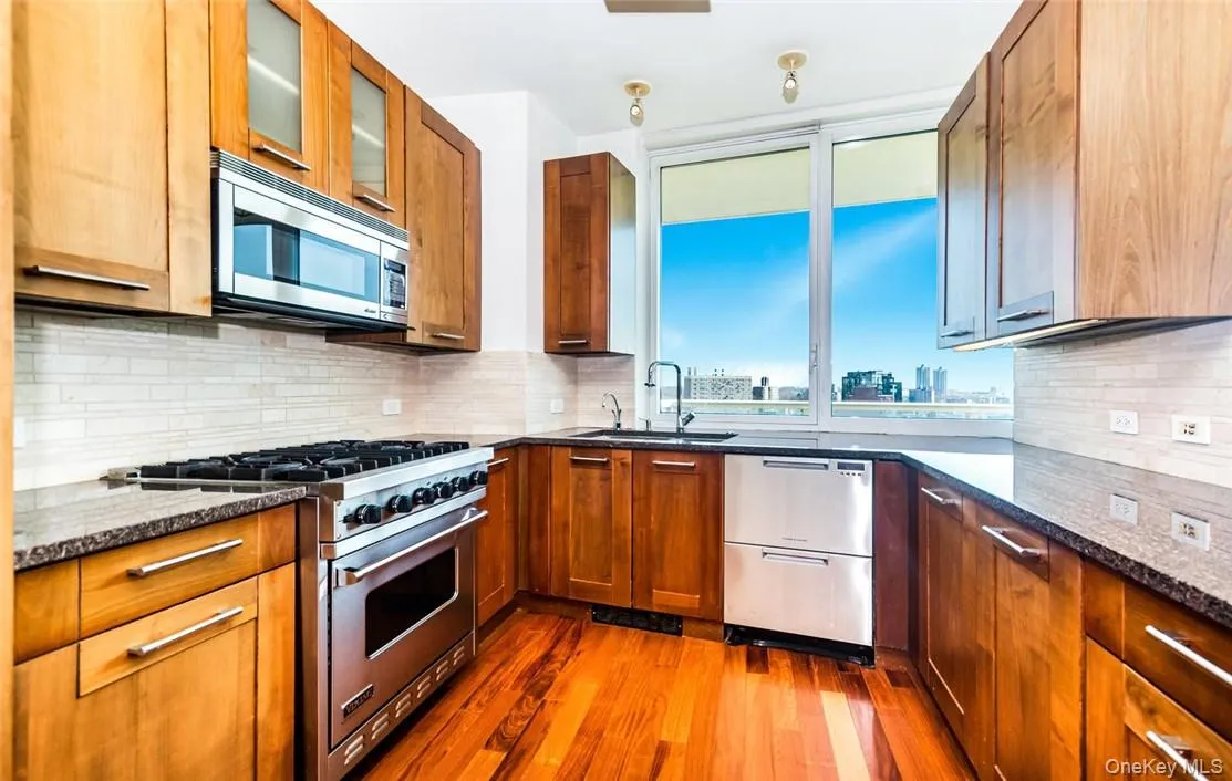 Kitchen with appliances with stainless steel finishes, dark hardwood / wood-style flooring, decorative backsplash, and sink Kitchen with appliances with stainless steel finishes, dark hardwood / wood-style flooring, decorative backsplash, and sink