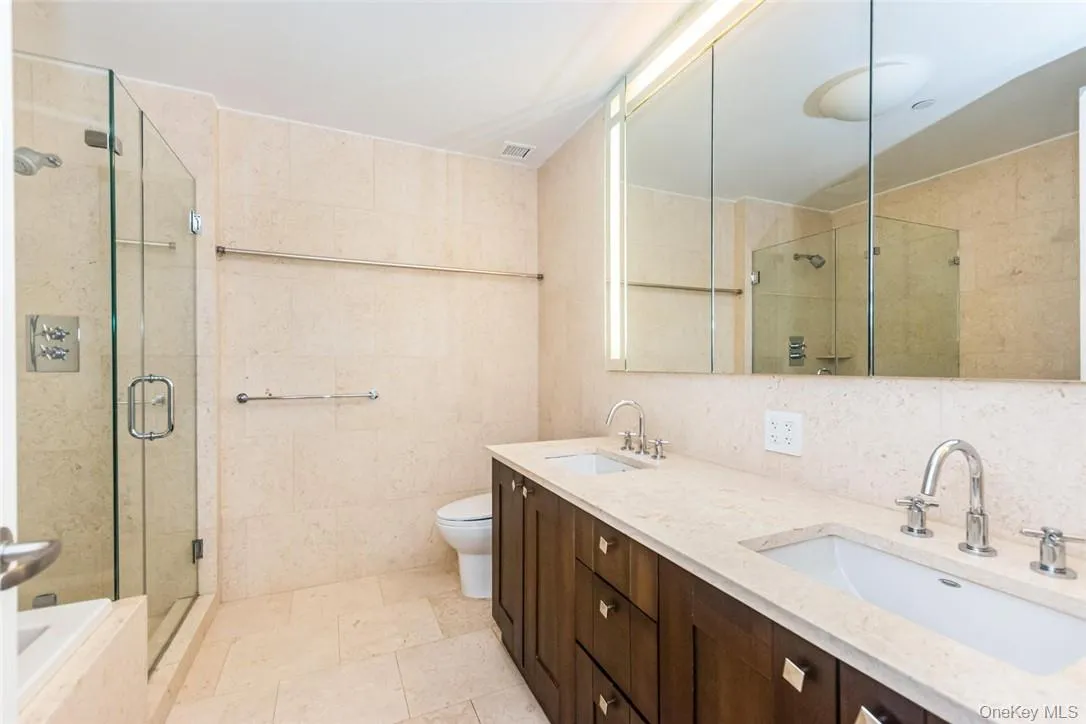 Full bathroom with tile walls, dual vanity, separate shower and tub, toilet, and tile patterned flooring Full bathroom with tile walls, dual vanity, separate shower and tub, toilet, and tile patterned flooring