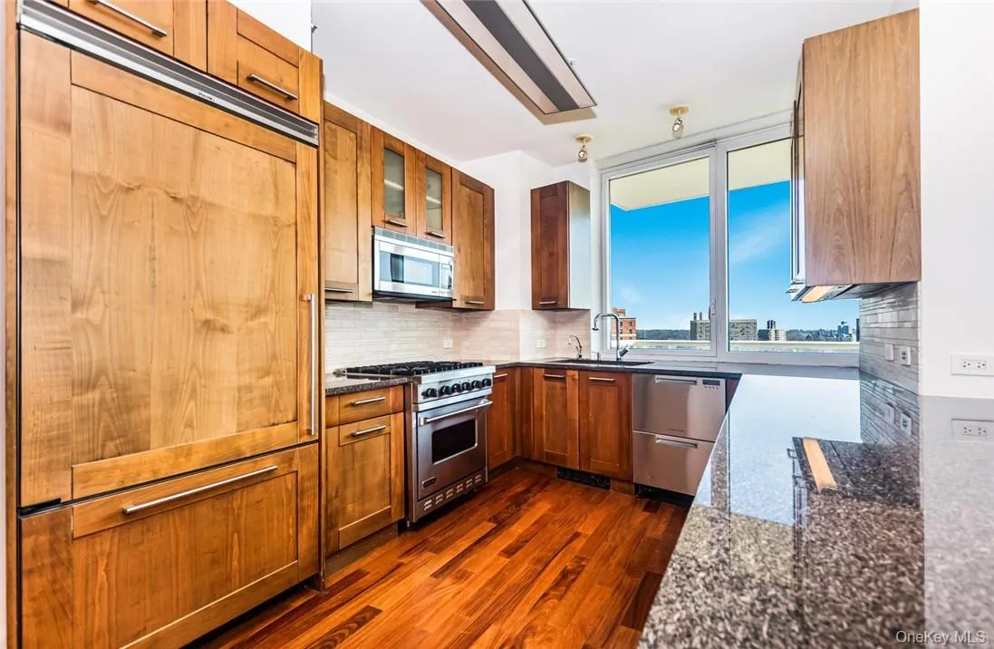 Kitchen featuring dark stone countertops, dark hardwood / wood-style flooring, decorative backsplash, high quality appliances, and sink Kitchen featuring dark stone countertops, dark hardwood / wood-style flooring, decorative backsplash, high quality appliances, and sink