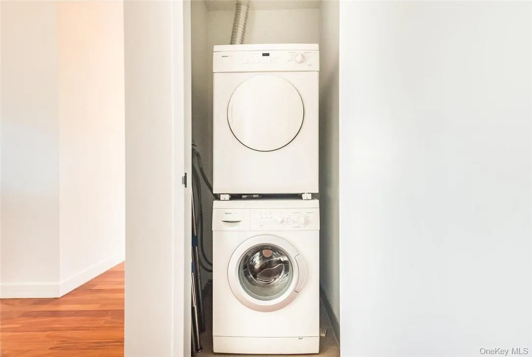 Clothes washing area featuring wood-type flooring and stacked washer / drying machine Clothes washing area featuring wood-type flooring and stacked washer / drying machine