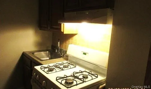 Kitchen featuring sink, decorative backsplash, stove, and wall chimney exhaust hood Kitchen featuring sink, decorative backsplash, stove, and wall chimney exhaust hood