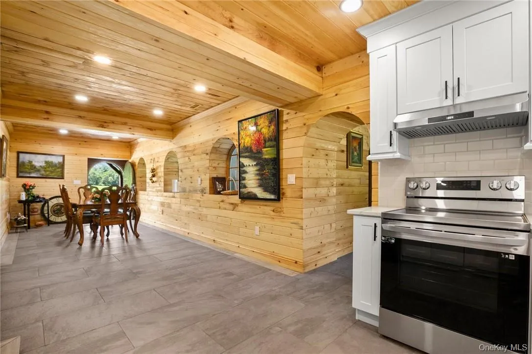 Kitchen featuring stainless steel range with electric stovetop, wood ceiling, white cabinetry, and wooden walls Kitchen featuring stainless steel range with electric stovetop, wood ceiling, white cabinetry, and wooden walls
