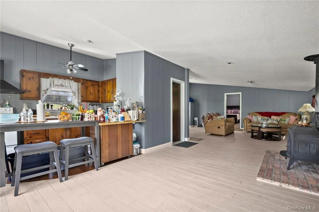 Kitchen featuring a textured ceiling, ceiling fan, a kitchen bar, wall chimney exhaust hood, and kitchen peninsula Kitchen featuring a textured ceiling, ceiling fan, a kitchen bar, wall chimney exhaust hood, and kitchen peninsula