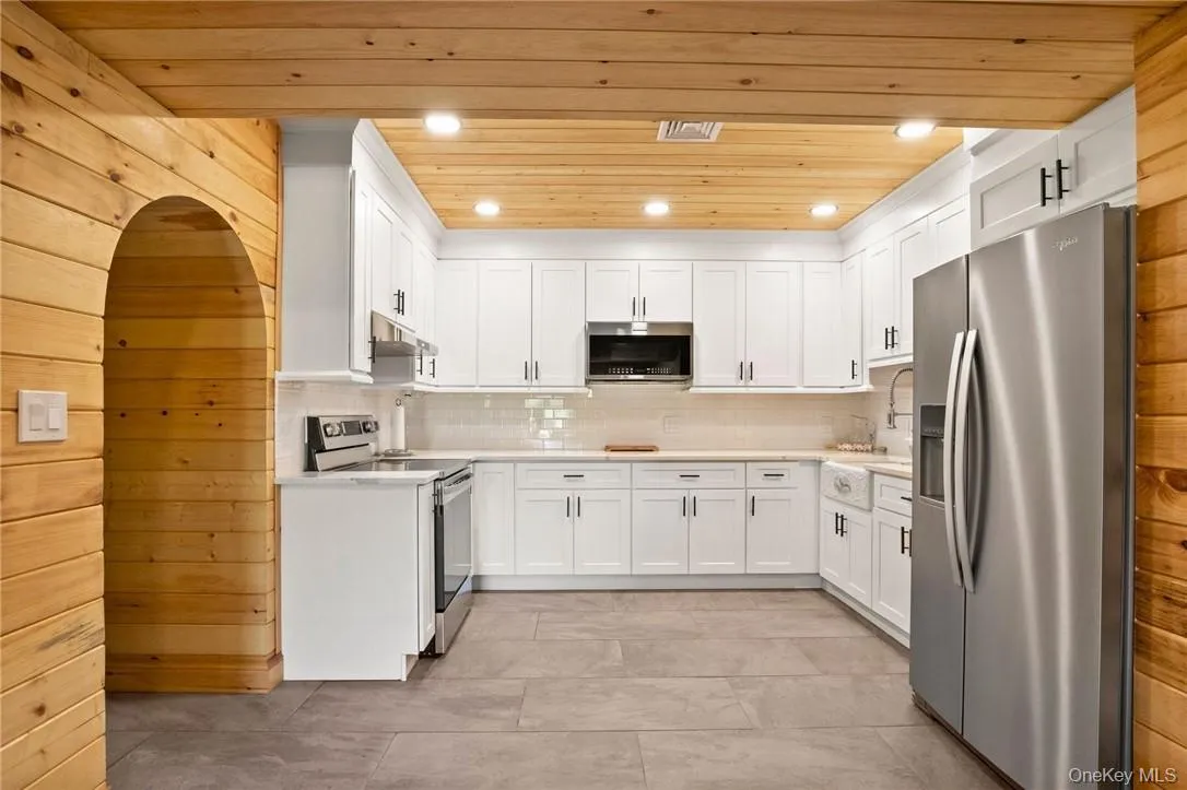 Kitchen featuring tasteful backsplash, appliances with stainless steel finishes, light tile patterned floors, white cabinets, and wood ceiling Kitchen featuring tasteful backsplash, appliances with stainless steel finishes, light tile patterned floors, white cabinets, and wood ceiling