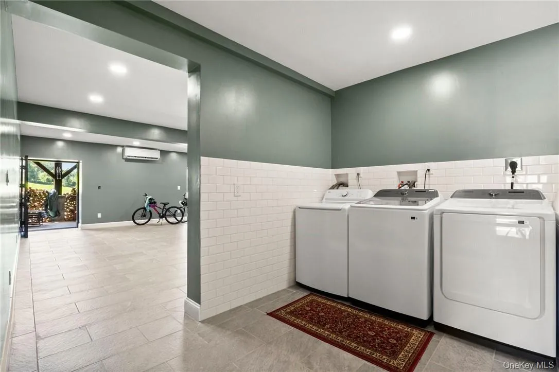Laundry room featuring washing machine and clothes dryer, a wall unit AC, tile walls, and light tile patterned floors Laundry room featuring washing machine and clothes dryer, a wall unit AC, tile walls, and light tile patterned floors