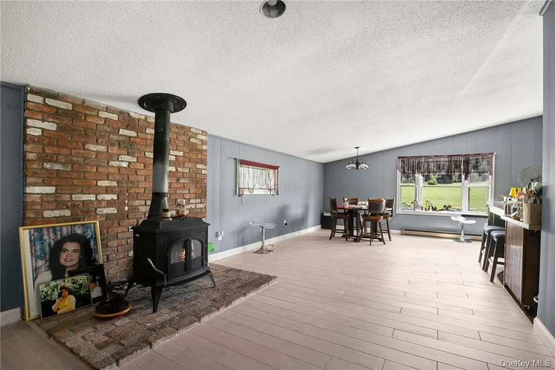 Living room featuring a textured ceiling, light hardwood / wood-style flooring, lofted ceiling, a chandelier, and a wood stove Living room featuring a textured ceiling, light hardwood / wood-style flooring, lofted ceiling, a chandelier, and a wood stove