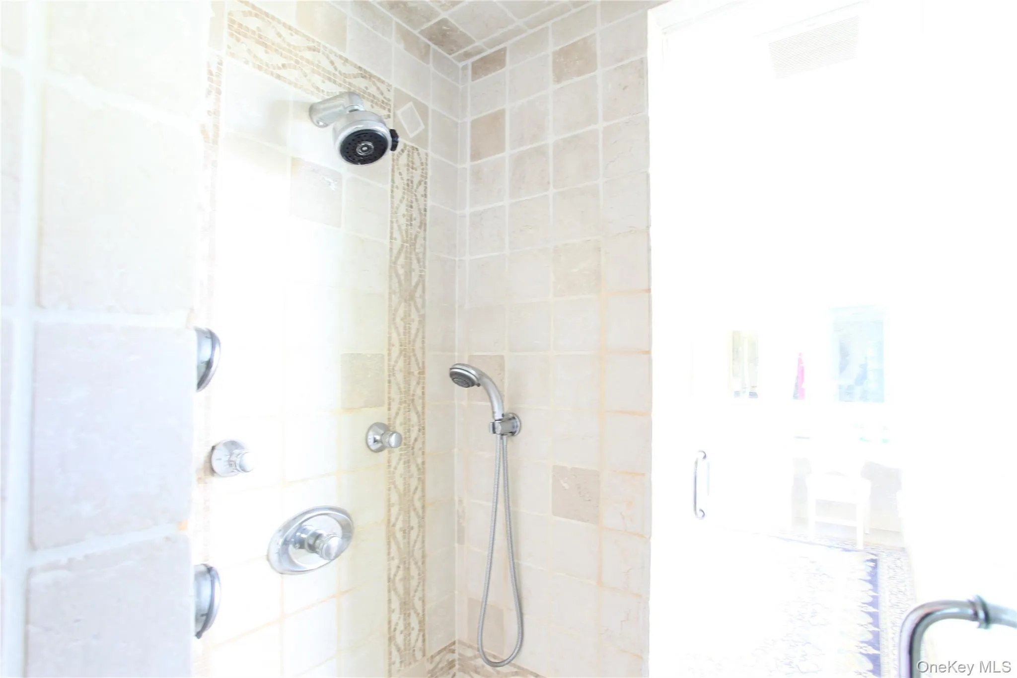 Shower stall featuring light-toned square wall tiles and a decorative vertical accent tile strip Shower stall featuring light-toned square wall tiles and a decorative vertical accent tile strip