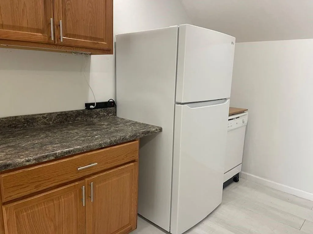 Kitchen featuring white appliances, lofted ceiling, dark stone countertops, and light hardwood / wood-style flooring Kitchen featuring white appliances, lofted ceiling, dark stone countertops, and light hardwood / wood-style flooring