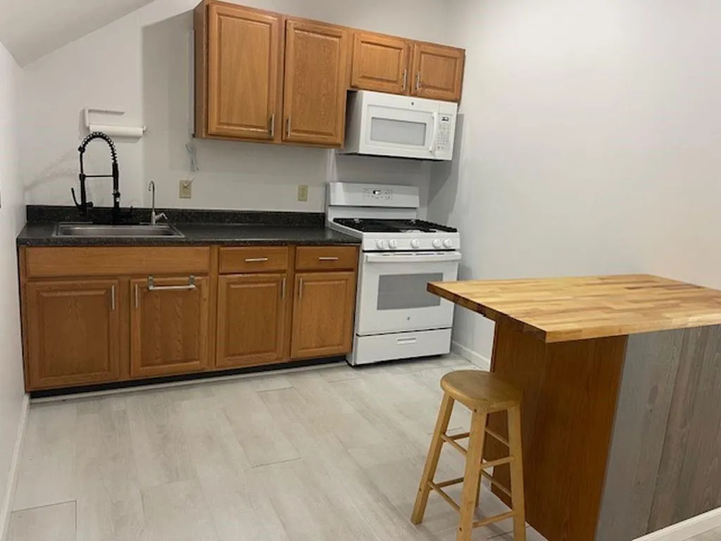 Kitchen featuring a kitchen bar, sink, light wood-type flooring, wood counters, and white appliances Kitchen featuring a kitchen bar, sink, light wood-type flooring, wood counters, and white appliances