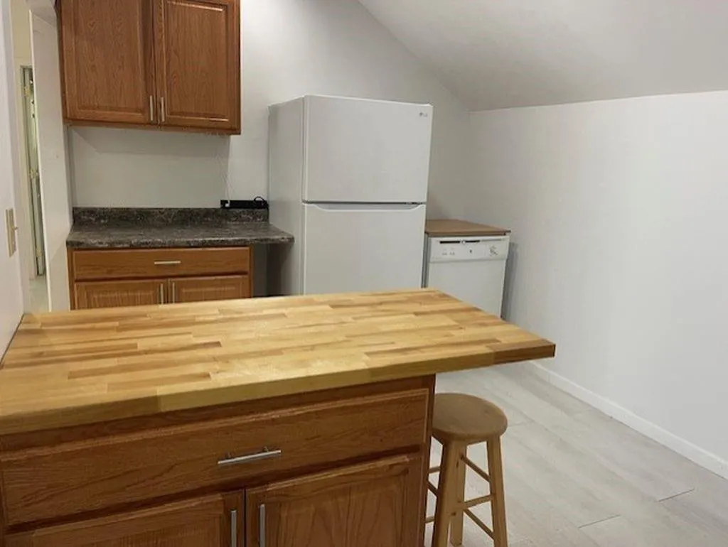 Kitchen featuring a kitchen breakfast bar, white appliances, light hardwood / wood-style floors, and butcher block counters Kitchen featuring a kitchen breakfast bar, white appliances, light hardwood / wood-style floors, and butcher block counters