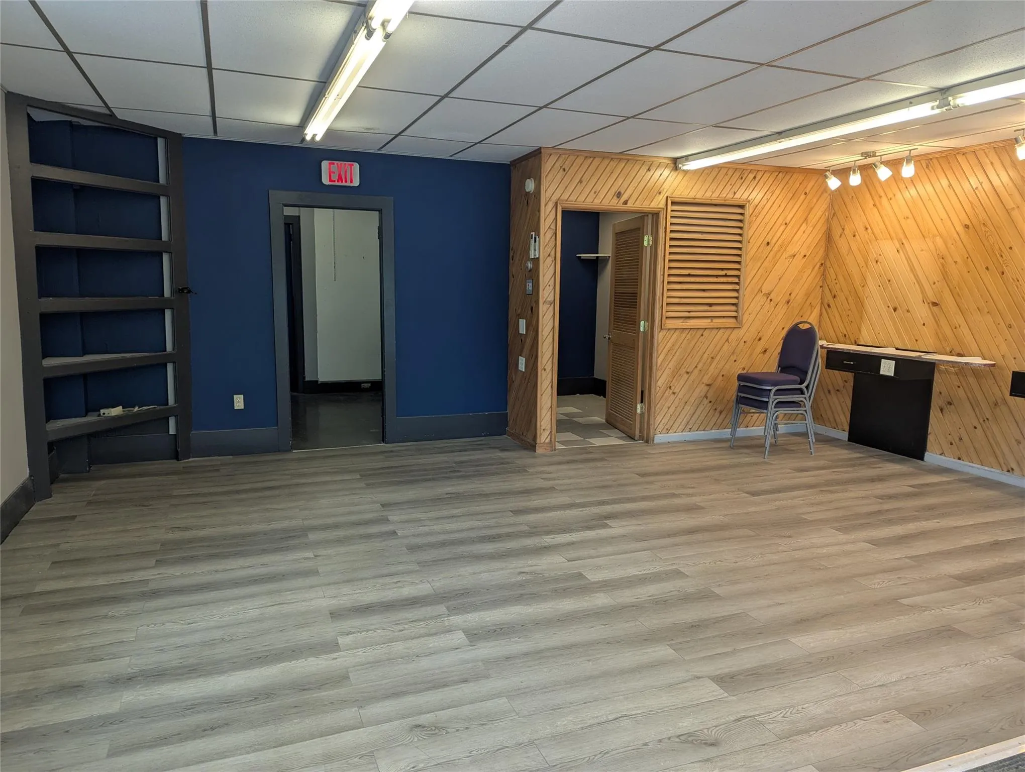 Unfurnished office featuring rail lighting, wooden walls, baseboards, and wood finished floors Unfurnished office featuring rail lighting, wooden walls, baseboards, and wood finished floors